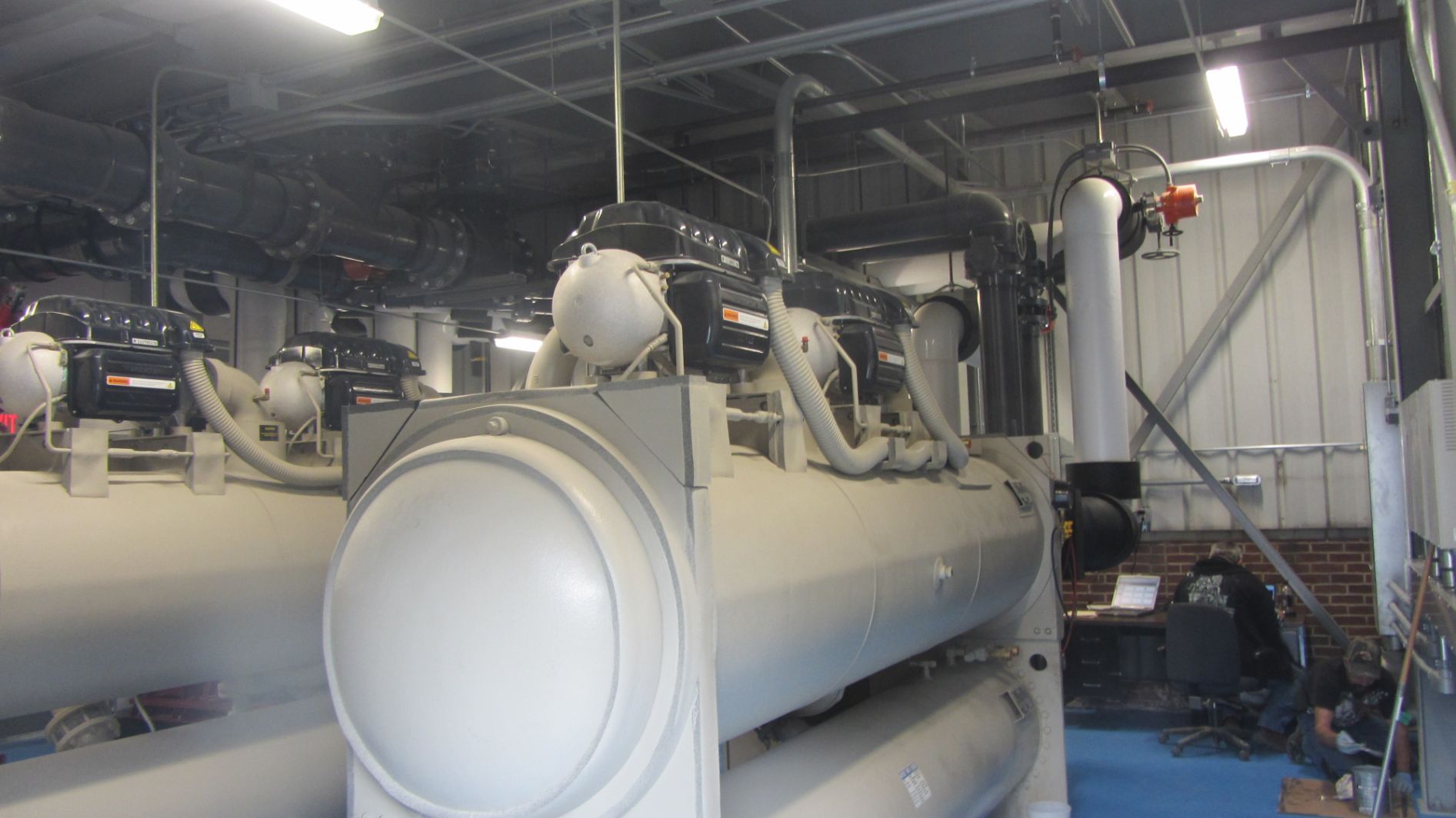 A large white machine in a room with pipes.